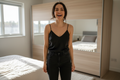 uma mulher vestida de Ice-Silk Camisole cor preta e uma calça jean preta, no quarto frente ao gurada roupa, feliz